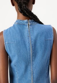Vestido sin mangas de mezclilla con un escote alto, que cuenta con un zipper trasero visible y un sutil pespunteado de contraste. Textura suave y de un azul claro.
