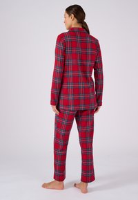 Conjunto de pijama de franela a cuadros rojos que incluye una parte superior de manga larga de corte holgado y pantalones a juego, con acentos en azul y negro en el patrón.