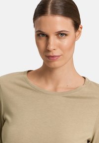 Blusa de manga larga color caqui con cuello redondo, textura suave y diseño ajustado, que cuenta con detalles sutiles y un acabado de tela suave.