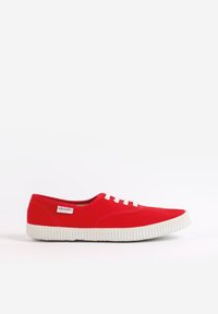 Zapatilla de lona roja con suela de goma blanca, que presenta cinco ojales y una pequeña etiqueta de marca en el lateral. Diseño clásico de caña baja.