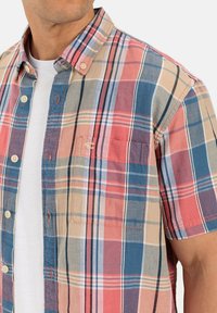 Korte mouwen geruite shirt van lichtgewicht stof. Heeft een combinatie van rode, blauwe en beige kleuren met een borstzak en knoopsluiting.