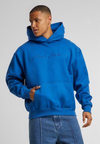 Felpa di cotone blu con tasca frontale, cappuccio con cordino e logo ricamato in blu scuro. Polsini e orlo a coste con una vestibilità rilassata.