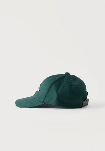 Σκούρο πράσινο καπέλο του μπέιζμπολ με μαύρο ρυθμιζόμενο λουράκι, εμφανιζόμενο από το πλάι σε απλό λευκό φόντο.