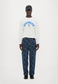 White long-sleeve shirt with blue "ICECREAM" print, paired with navy pants featuring repeated text pattern, and black shoes.