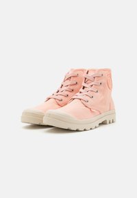 Zapatillas altas de lona rosa claro con cierre de cordones, suelas de goma beige y acentos texturizados en los laterales y en la parte trasera.