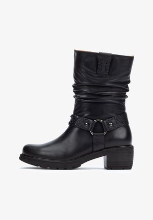 Botte de cheville en cuir noir avec un tige plissée, une sangle texturée avec des détails en métal, et un talon épais. Semelle en caoutchouc plate pour une meilleure durabilité.