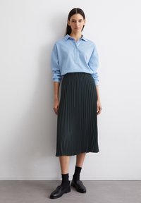 Hellblaues Button-down-Hemd kombiniert mit einem dunklen, gefalteten Midirock. Schwarze Slippers und Knöchelsocken runden das Outfit ab.