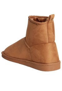 Botas de tobillo marrones con una textura suave similar al ante, forma de punta redondeada, diseño de bajo perfil y un pequeño acento decorativo en la parte posterior.
