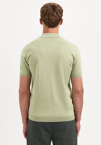 Korte mouwen poloshirt in lichtgroen, gebreide textuur, strak ontwerp, geribde kraag en zoom, gezien vanaf de achterkant.