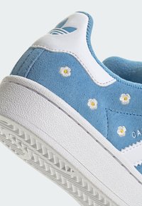 Sneaker blu in camoscio con accenti bianchi, caratterizzato da margherite ricamate sulla tomaia e una suola bianca testurizzata con un battistrada decorato.