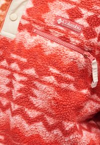 Κόκκινο πουλόβερ από φλις με μοτίβο σε σχήμα ζιγκ-ζαγκ, που διαθέτει κρεμ πόλο μ ε κουμπιά και τσεπη με φερμουάρ. Μαλακή υφή με αντίθετα εξαρτήματα.