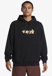 Sudadera negra de tejido suave con un gráfico floral naranja en el pecho. Cuenta con un bolsillo tipo canguro y capucha con cordón.