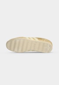 Μπεζ σόλα αθλητικού παπουτσιού Adidas Japan με σχέδιο πέλματος σε σχήμα ψαροκόκκαλο και λογότυπο Adidas, εμφανιζόμενη σε λευκό φόντο.