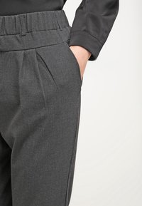 Harmaat räätälöidyt housut, joissa on pleatattu muotoilu, pehmeä pinta ja joustava vyötärö, kädet sivutaskuissa.