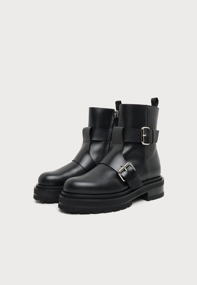 Bottines en cuir noir avec semelles épaisses, fermeture éclair latérale et deux boucles argentées sur le devant et la cheville.