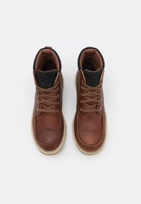 Bottes de cheville en cuir marron avec des accents noirs, dotées de lacets beige, d'une finition texturée et d'une semelle claire.