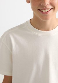 T-shirt beige chiaro a maniche corte realizzato in tessuto morbido, con scollatura rotonda e dettagli di cucitura sottili. Texture liscia, design casual.