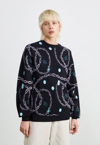 Sweater de malha preta com um padrão geométrico em roxo claro e verde-azulado, com decote redondo e punhos canelados, oferecendo uma aparência texturada.