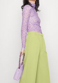 Fialový svetřík s dlouhým rukávem a rolákem, zdobený malým květinovým vzorem, doplněný vysokým pasem a širokými zelenými kalhotami a levandulovou kabelkou s řetízkovým popruhem.