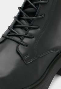 Μαύρο δερμάτινο μπότες με λεία επιφάνεια, σχέδιο με κορδόνια, ενισχυμένα κατσαβίδια και μικρή ανυψωμένη φτέρνα. Ραφές κατά μήκος των πλευρών.