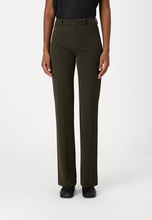 Pantalon slim taille haute vert olive pailleté porté avec des chaussures noires et un top noir sans manches sur une personne debout.