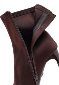 Bottine en satin marron avec un bout pointu et un talon aiguille. Présente une fermeture éclair sur le côté et une texture lisse. Doublure intérieure visible avec un pli.
