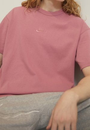 Camiseta de algodón rosa con un corte relajado, que presenta un logo bordado de Nike en el pecho. Mangas cortas y cuello redondo.