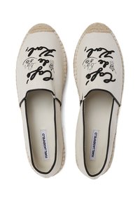Bézs vászon espadrilles fekete nyomtatott szöveggel és illusztrációkkal, kontrasztos fekete díszítéssel és fonott juta talppal.