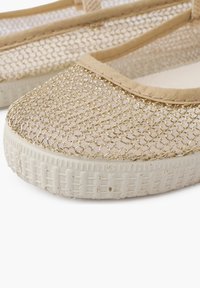 Bailarinas de malla beige con un patrón de hilo dorado, ribete de tela y una suela de goma blanca texturizada. Presentan un diseño de punta redondeada.