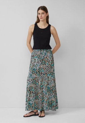 Haut sans manches noir associé à une longue jupe à motifs présentant des formes géométriques en turquoise, marron et blanc. Des sandales plates sont portées.