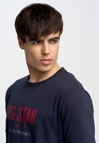 Camiseta de algodón en color marino con mangas cortas, que presenta el texto rojo "BIG STAR" y texto adicional en blanco debajo, cuello redondo y un diseño minimalista.
