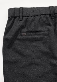 Svarta texturerade byxor med en slät finish. Har bälteshällor, en liten bakficka och en diskret varumärkesetikett sydd på fickan.