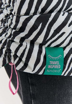Black and white zebra print fabric with gathered stitching and a green tag reading "Travel Inspired Naoko" attached to dark denim.