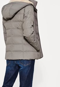 Grå isoleret jakke med hætte, quiltet design og en blød, lyse farvet foring. Parret med mørkeblå jeans.