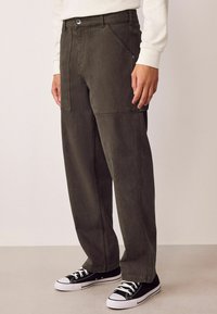 Pantalons larges en denim vert foncé, dot�és de coutures doubles, de poches latérales et d'une fermeture à boutons, associés à des baskets noires.