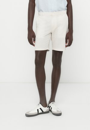 Light beige linen shorts with a relaxed fit, featuring a flat front and a smooth texture, paired with gray and black sneakers.