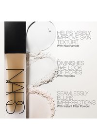 Flacon de fond de teint liquide avec des gouttes de poudre et de sérum montrant les bienfaits : améliore la texture de la peau, diminue les pores, atténue les imperfections.
