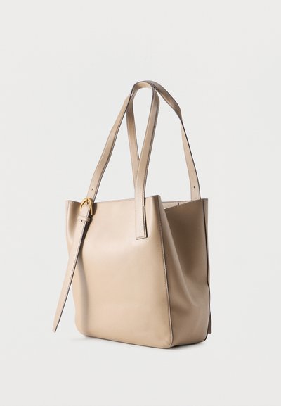 Μπεζ δερμάτινη τσάντα ώμου με δύο μακριά χερούλια και ρυθμιζόμενο λουρί με χρυσή αγκράφα, εμφανίζεται πάνω σε ένα απλό ανοιχτόχρωμο φόντο.