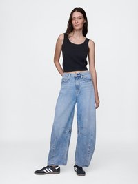 Svart kort tanktopp, lyseblå vide jeans med slitte detaljer, og svarte sneakers med hvite striper, på en nøytral bakgrunn.