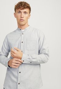 Hele halli, pika varrukaga nööpidega särk mandariini kraega, rinna tasku ja pruunide nööpidega. Kangas on peene tekstuuriga.