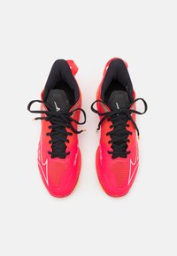 Red athletic shoes with black accents, featuring a mesh upper, black laces, and logo details. Lightweight design with rubber outsole.