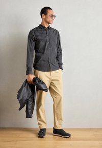 Striped black button-up shirt, beige trousers, black leather jacket, and black sneakers. Smooth fabric and tailored fit with a neat collar.