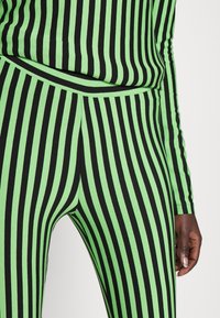 Zielone i czarne legginsy w paski o dopasowanym kroju i miękkiej fakturze, z pionowymi liniami tworzącymi wyrazisty wzór.