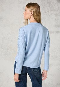 Hellblaues Sweatshirt mit langen Ärmeln, das über strukturierte Akzente an den Ärmeln und einen lässigen Schnitt verfügt. Weiches, gestricktes Material mit minimalistischen Design.