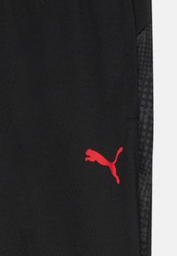 Svarte treningseire med strukturert stoff, med en rød Puma-logo og et mønstrete mørkt sidepanel.