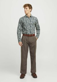 Chemise à boutons bleu marine avec un motif floral blanc ; associée à un pantalon plissé marron ; ceinture marron ; chaussures avec une finition texturée.