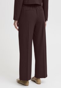 Brown, wide-leg trousers with elastic waistband, featuring two back pockets and a smooth, tailored texture. Worn with light-colored loafers.