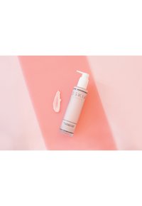 Oskia Renaissance Body Treatment Milk i en frostad pumpflaska med vit kork. Hällt kräm på en rosa yta, slät konsistens, lätt design.