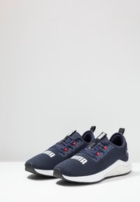 Námořnicky modré sportovní tenisky s texturovanou síťovinou, bílou mezipodešví, červenými akcenty a odtahovým poutkem pro snadné obouvání. Vyznačuje se výrazným logem.