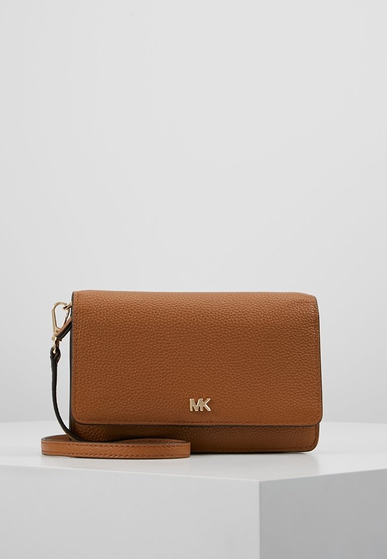 Pochette bracelet en cuir marron texturé avec un fermoir doré et un petit logo MK doré à l'avant, posé sur une surface blanche.